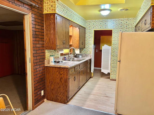 1440 Southwood Dr, Lima, OH 45805 - kitchen featuring freestanding refrigerator, a sink, light countertops, brown cabinets, and wallpapered walls