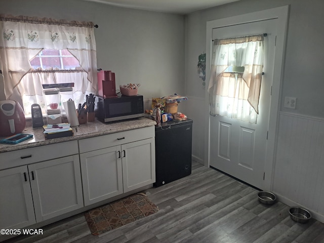 kitchen with black microwave, wainscoting, light wood-style flooring, white cabinetry, and fridge