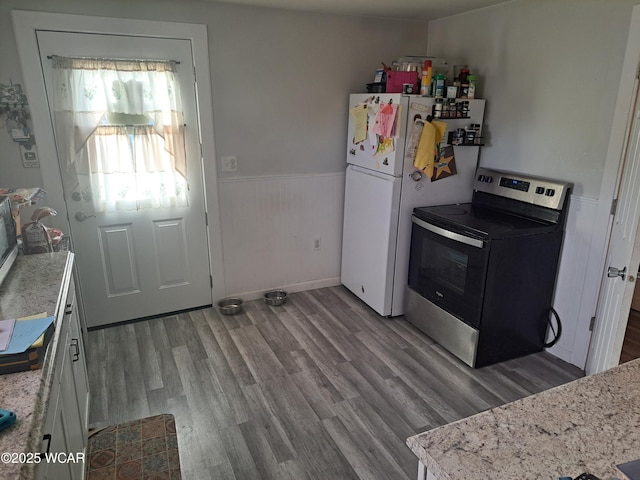 kitchen featuring light stone countertops, stainless steel range with electric stovetop, wood finished floors, and wainscoting