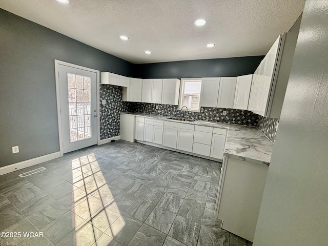 kitchen with sink, light stone counters, a textured ceiling, white cabinets, and tasteful backsplash