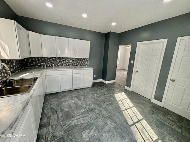 kitchen featuring white cabinetry, sink, light stone countertops, and decorative backsplash