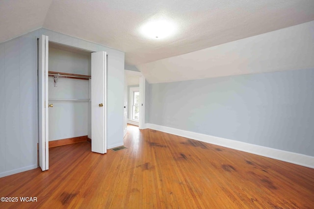 unfurnished bedroom featuring baseboards, vaulted ceiling, visible vents, and wood finished floors