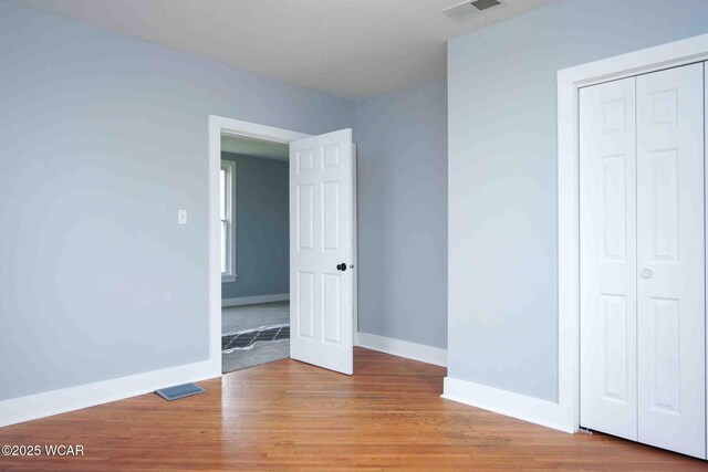 unfurnished bedroom featuring wood finished floors, a closet, baseboards, and visible vents