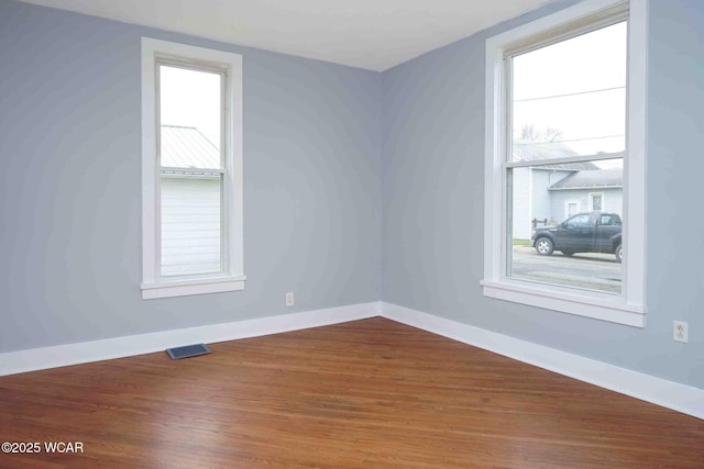 empty room with baseboards, visible vents, and wood finished floors
