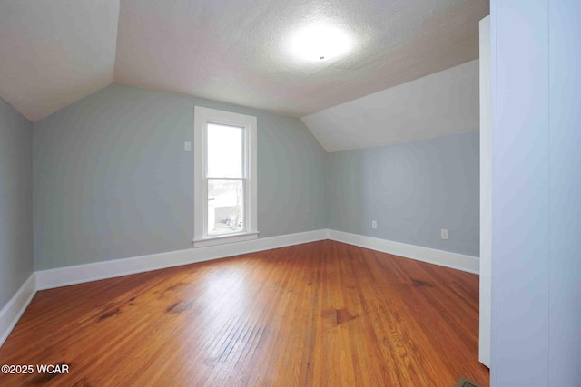 additional living space featuring baseboards, lofted ceiling, a textured ceiling, and wood-type flooring