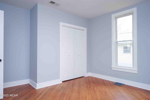 unfurnished bedroom with a closet, baseboards, visible vents, and wood finished floors