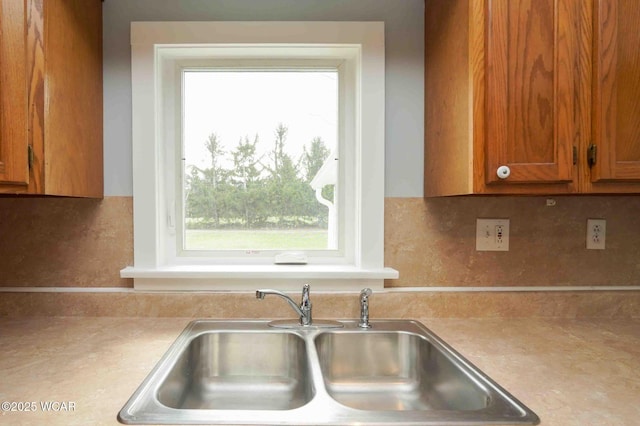 kitchen with backsplash, light countertops, a sink, and brown cabinetry