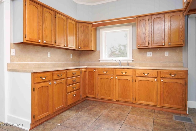 kitchen featuring light countertops, a sink, brown cabinets, and visible vents