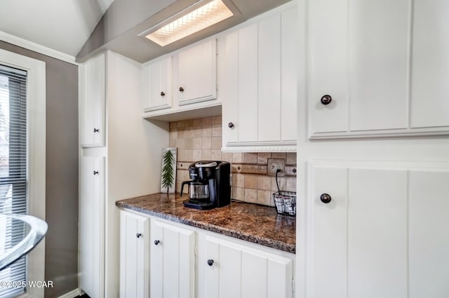 kitchen featuring tasteful backsplash, dark stone countertops, white cabinetry, and vaulted ceiling