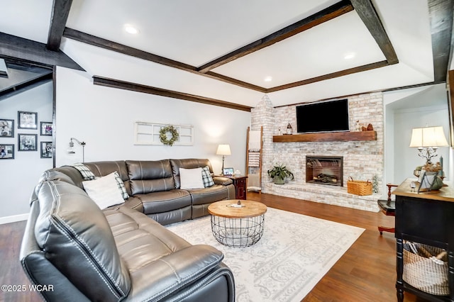 living room featuring beamed ceiling, a brick fireplace, baseboards, and wood finished floors