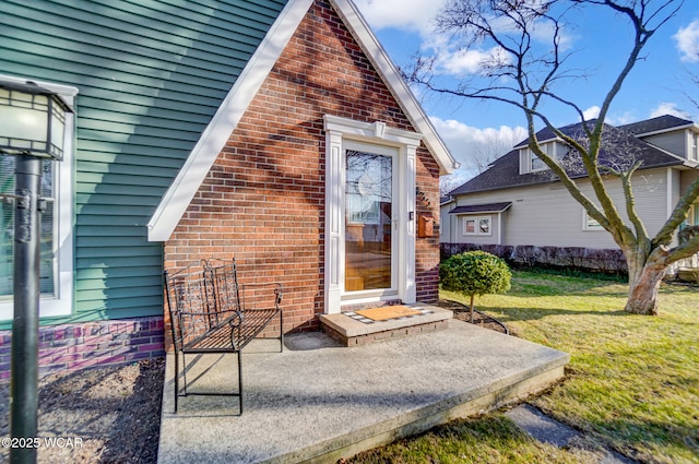 view of exterior entry featuring brick siding and a yard