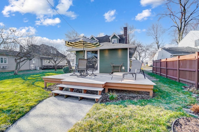 back of property with a deck, a lawn, fence, and a chimney