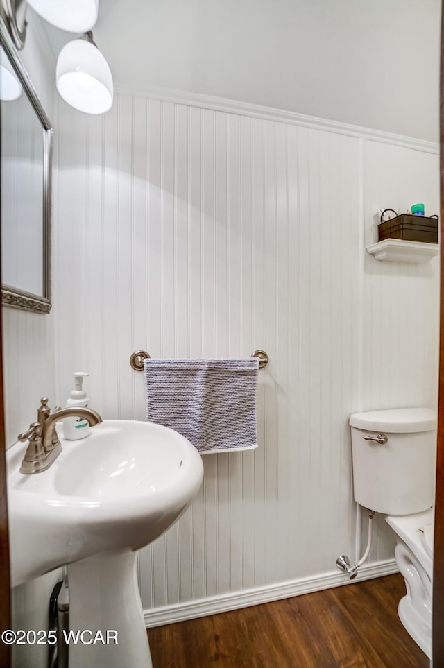 bathroom with toilet, wood finished floors, baseboards, and a sink