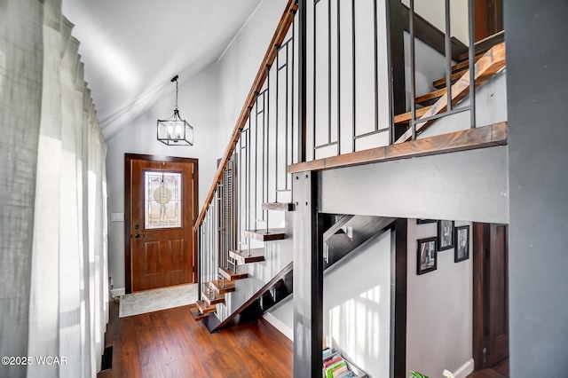 foyer featuring baseboards, stairs, lofted ceiling, hardwood / wood-style floors, and an inviting chandelier