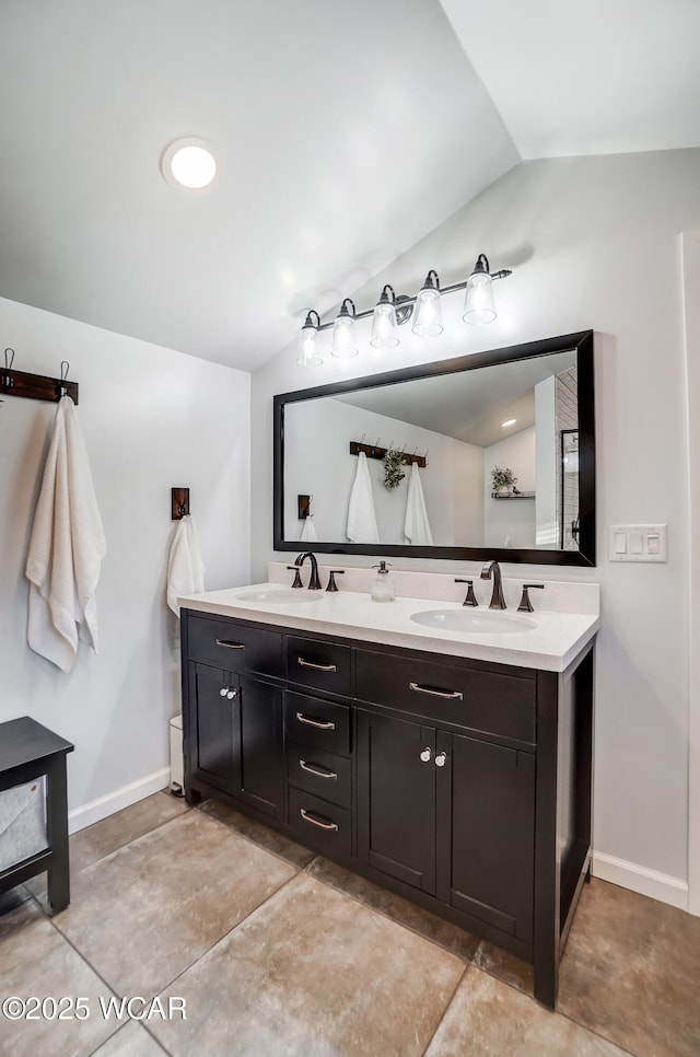 bathroom featuring lofted ceiling, double vanity, baseboards, and a sink