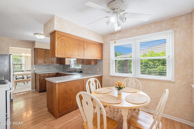 2069 High Ridge Rd, Lima, OH 45805 - kitchen with range, a peninsula, brown cabinets, light wood-style floors, and freestanding refrigerator