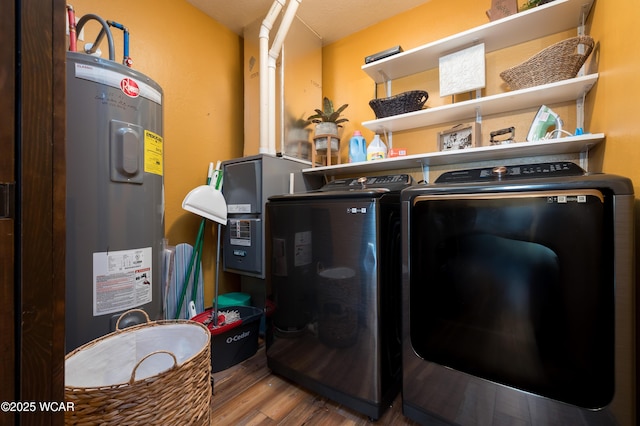 clothes washing area with laundry area, washing machine and dryer, wood finished floors, and electric water heater