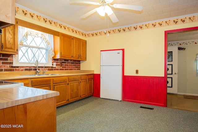 kitchen with white refrigerator, crown molding, sink, and light carpet