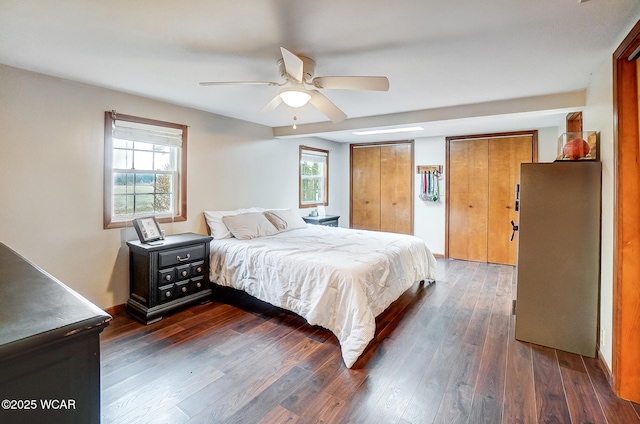 bedroom featuring dark wood-type flooring, ceiling fan, and multiple closets