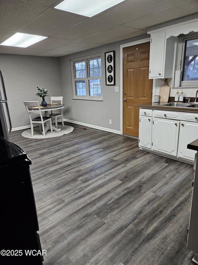 kitchen with dark countertops, dark wood-style flooring, white cabinets, and a sink