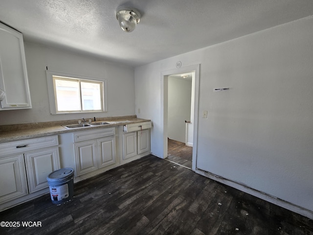 kitchen with light countertops, dark wood-type flooring, white cabinetry, a sink, and a textured ceiling