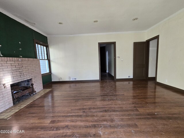 unfurnished living room featuring a brick fireplace, dark wood-style flooring, crown molding, and baseboards