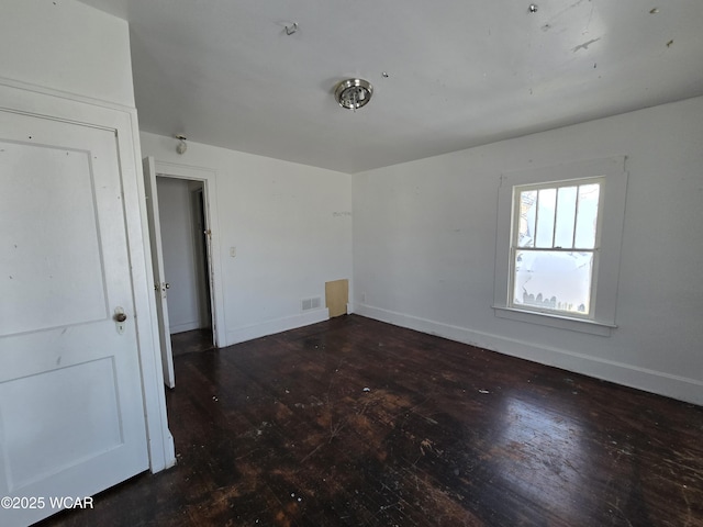 spare room with dark wood finished floors, visible vents, and baseboards