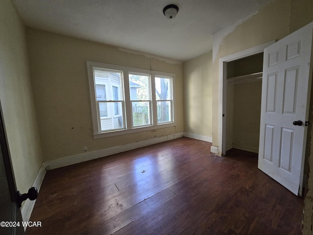 unfurnished bedroom with a closet, dark wood-style flooring, and baseboards