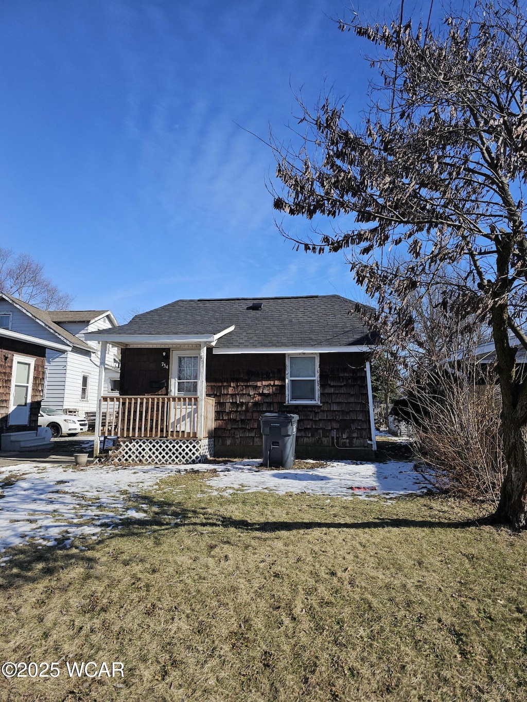 rear view of house with a lawn and roof with shingles