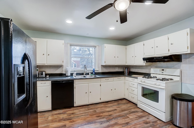 kitchen with under cabinet range hood, dark countertops, black appliances, and a sink