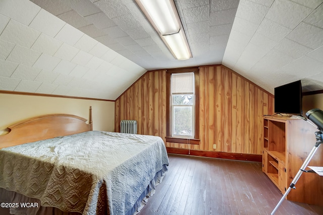 bedroom with hardwood / wood-style flooring, radiator heating unit, wooden walls, baseboards, and vaulted ceiling