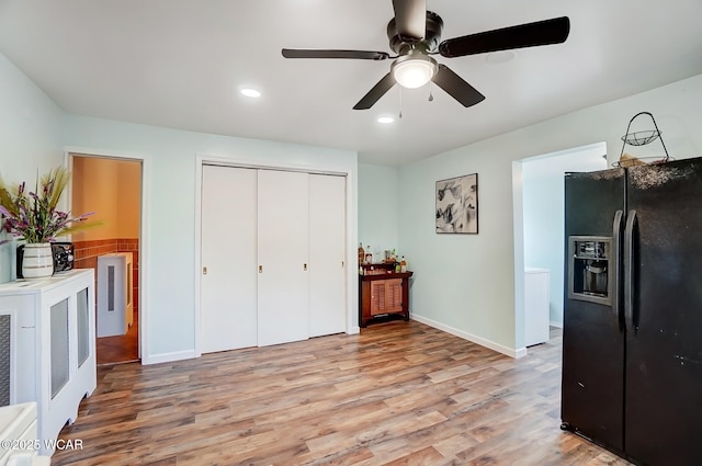 bedroom featuring light wood finished floors, black fridge, ensuite bath, and a closet