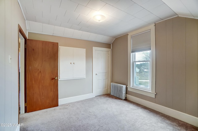 unfurnished bedroom featuring baseboards, lofted ceiling, radiator, and carpet floors