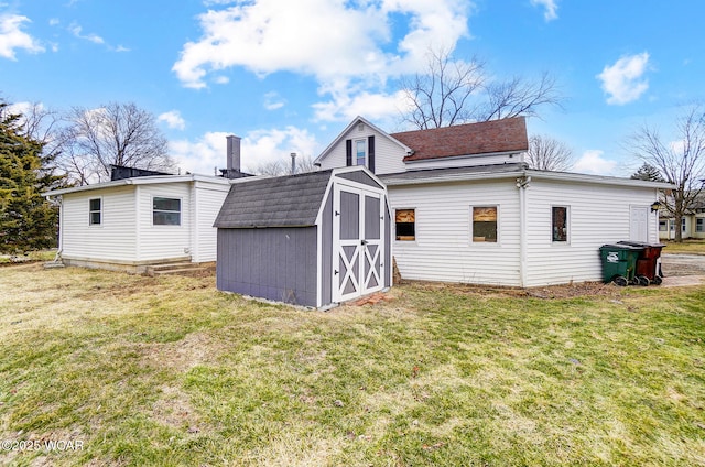 rear view of property with a storage shed, a lawn, an outdoor structure, and a shingled roof