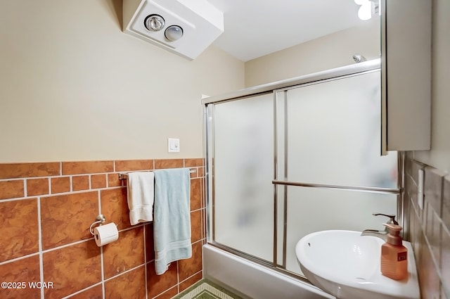 bathroom featuring tile walls, enclosed tub / shower combo, and a sink