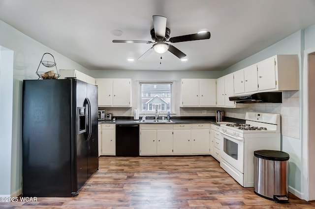 kitchen featuring dark countertops, tasteful backsplash, under cabinet range hood, black appliances, and a sink