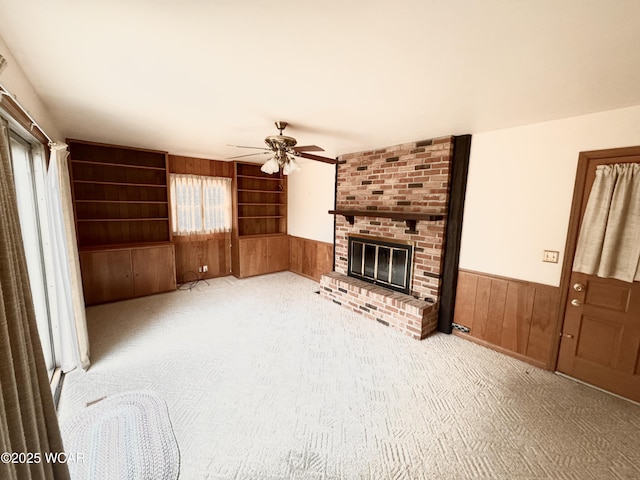 living room with wainscoting, ceiling fan, carpet flooring, wood walls, and a brick fireplace