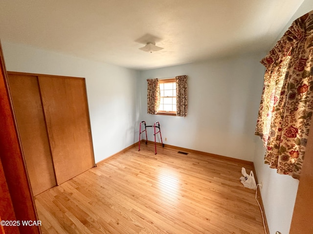 unfurnished bedroom featuring light wood finished floors, baseboards, visible vents, and a closet