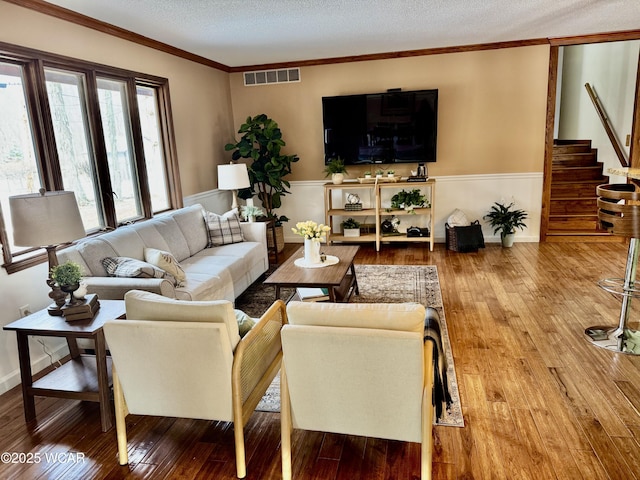 living area featuring a textured ceiling, wood finished floors, visible vents, ornamental molding, and stairway