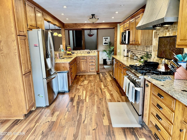 kitchen with light stone counters, stainless steel appliances, premium range hood, a sink, and brown cabinetry