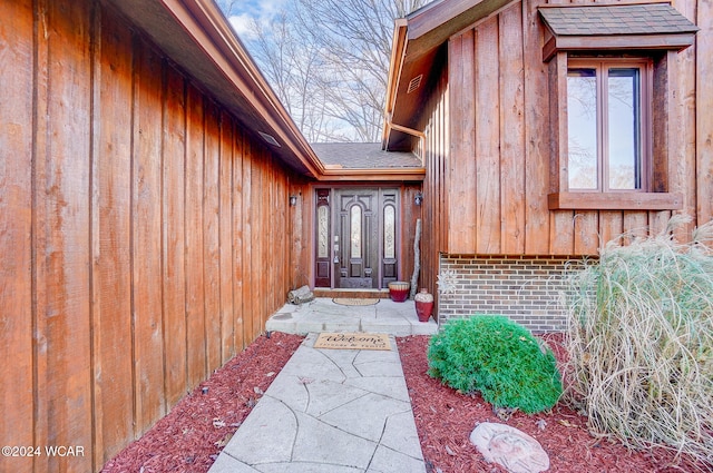 entrance to property featuring board and batten siding and roof with shingles