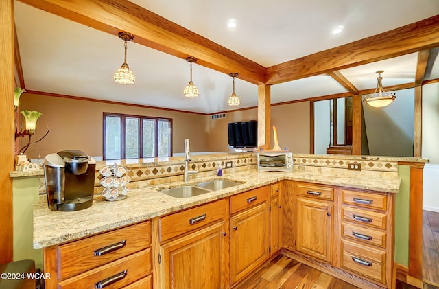 kitchen with light stone counters, light wood-style flooring, a sink, tasteful backsplash, and decorative light fixtures