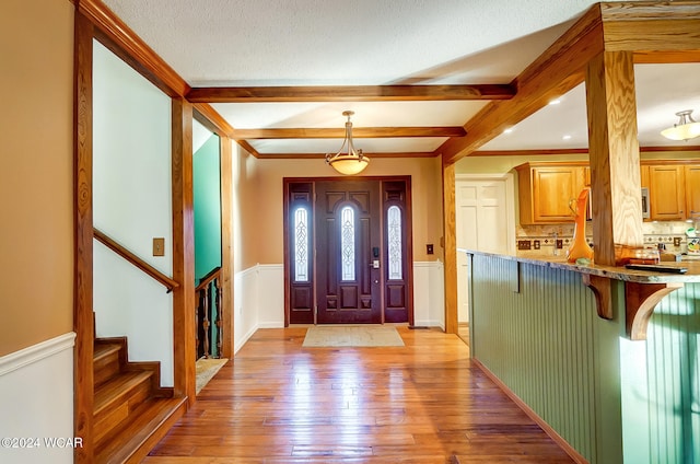 entryway with a textured ceiling, stairway, wainscoting, light wood-type flooring, and beam ceiling