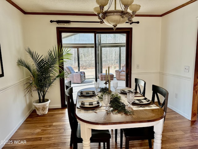 dining area featuring crown molding, an inviting chandelier, a textured ceiling, wood finished floors, and baseboards