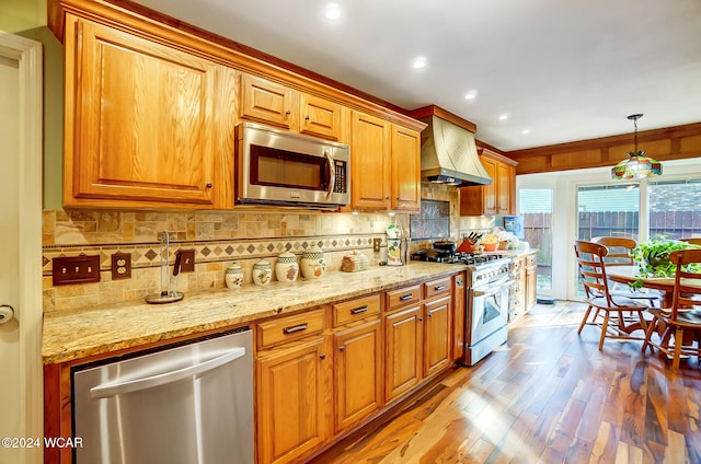 kitchen with light wood finished floors, decorative backsplash, custom exhaust hood, stainless steel appliances, and pendant lighting