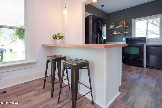 kitchen with black appliances, a kitchen bar, dark wood-type flooring, and hanging light fixtures