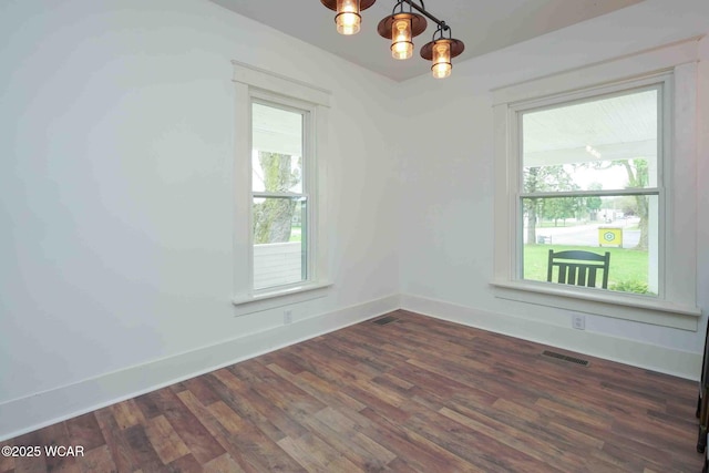 spare room featuring a chandelier, plenty of natural light, dark wood finished floors, and baseboards