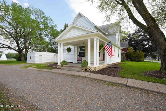 view of front of house featuring covered porch, a front lawn, a shingled roof, and a detached garage