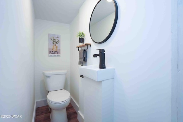 half bathroom with wood finished floors, toilet, and baseboards