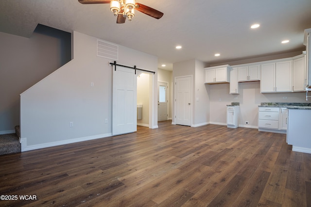 kitchen featuring ceiling fan, light stone counters, white cabinets, dark hardwood / wood-style flooring, and a barn door